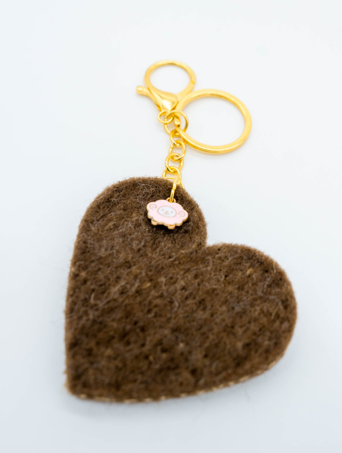 A brown felt heart-shaped keychain with a gold-tone metal clasp and a small pale pink flower charm, shown on a plain white background.