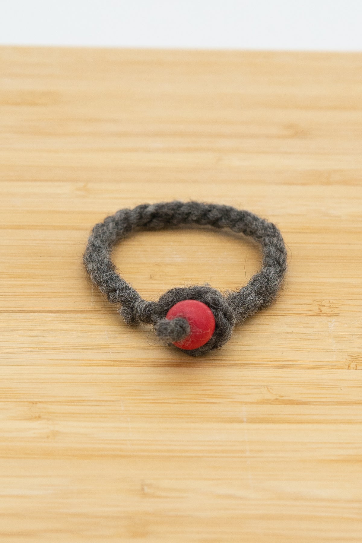 Charcoal gray wool bracelet handmade from Mooskit the Shetland ram on a light wooden background 
