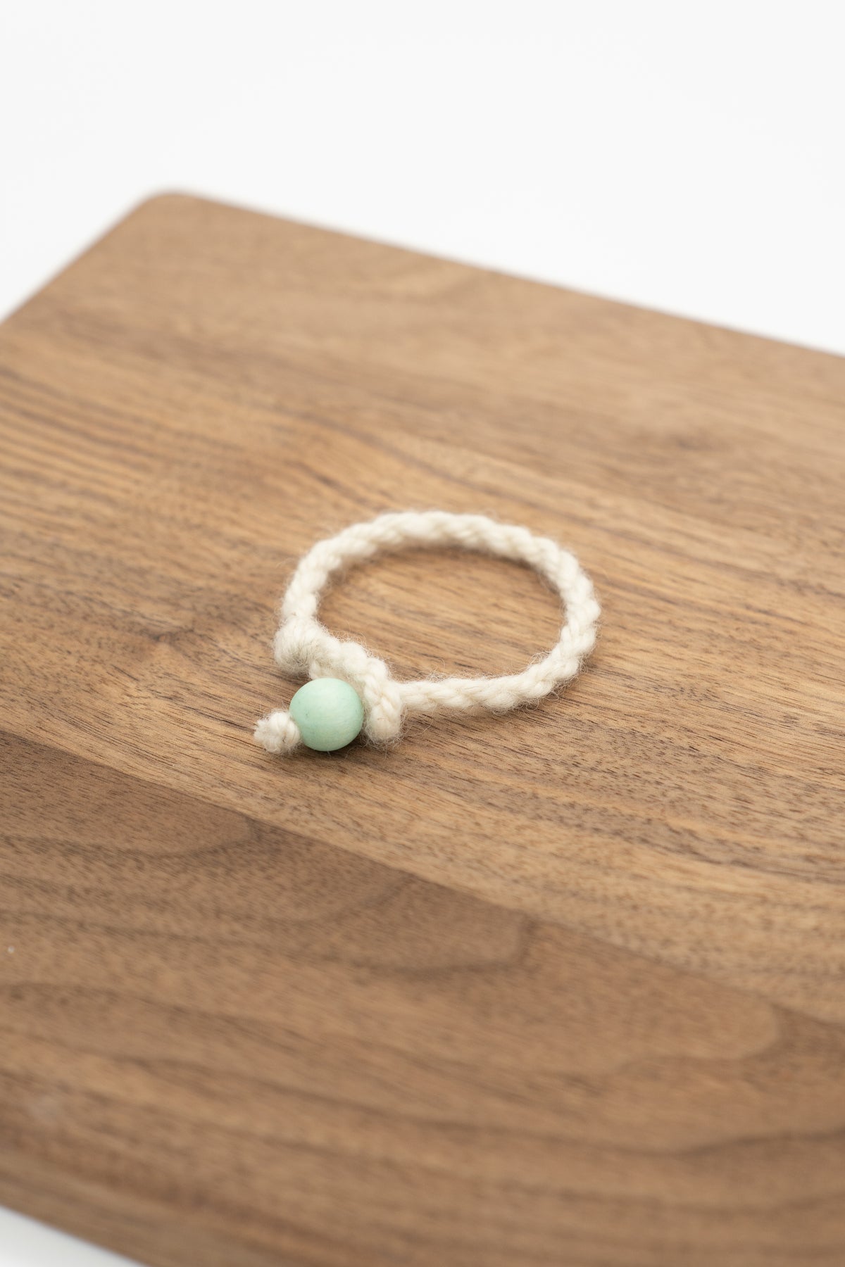 White wool bracelet from Valkia the Finnsheep with light green bead on a wooden background 