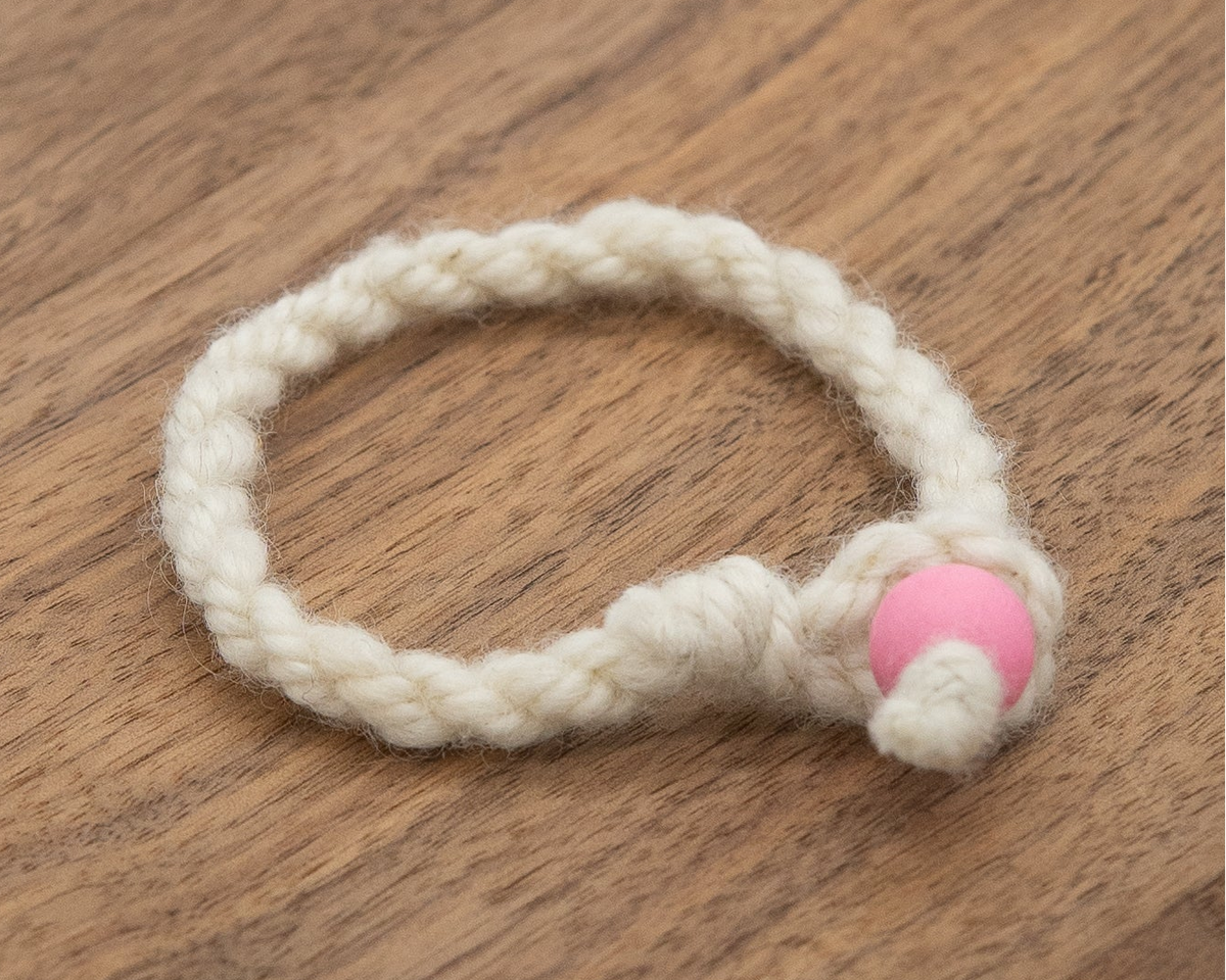Valkia the Finnsheep's white wool bracelet with a pink bead on a wooden background 